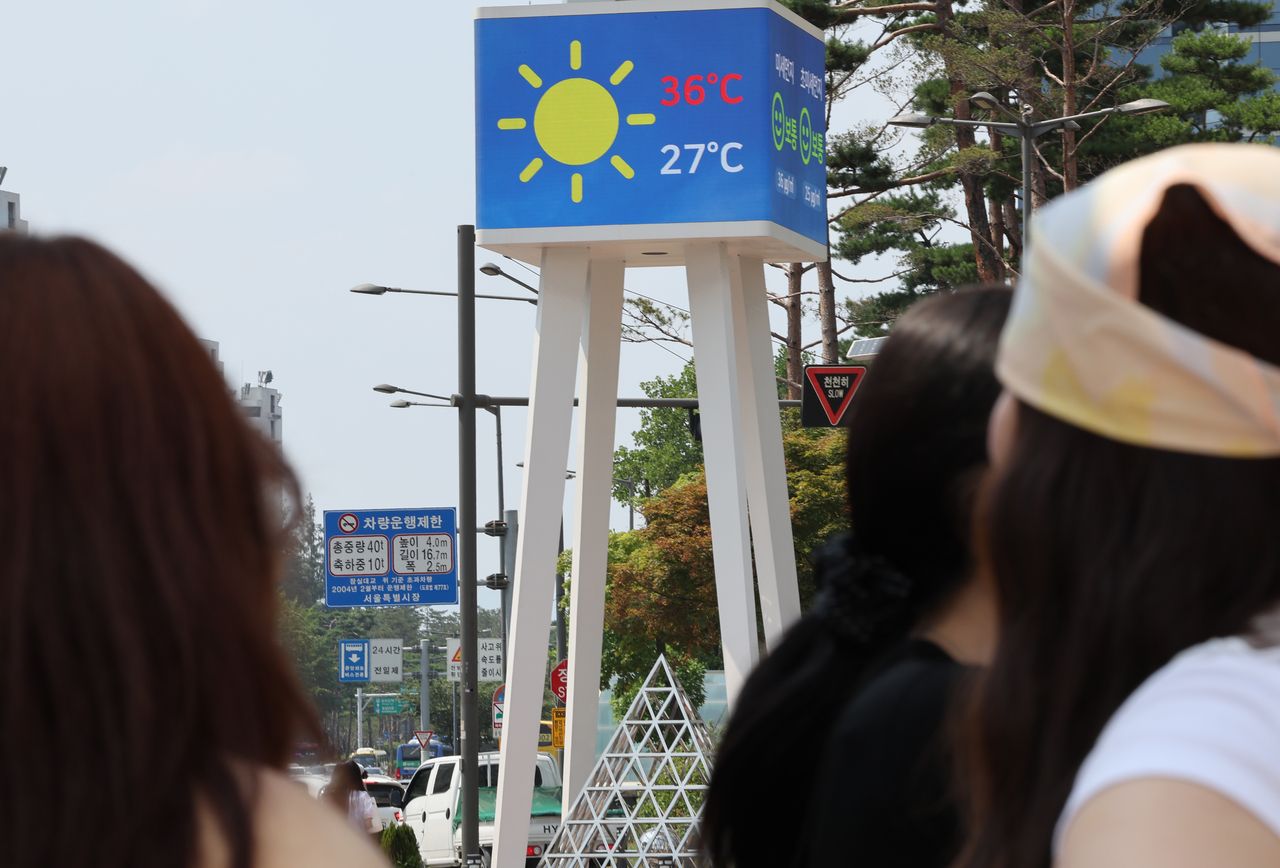 Pedestrians on Tuesday walk past a digital thermometer in Songpa-gu in southern Seoul that shows a temperature reading of 36 degrees Celsius. (Yonhap)]