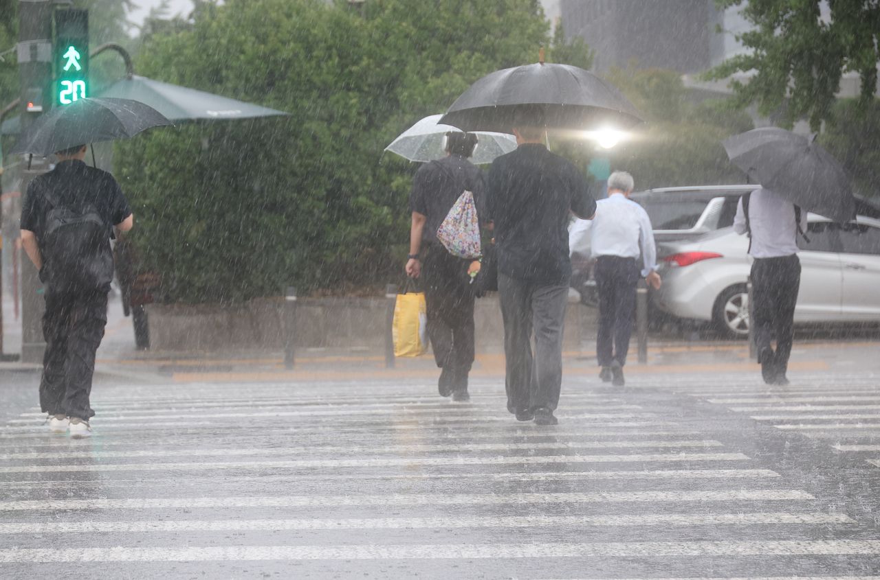 People cross a crosswalk with umbrellas near the National Assembly in Seoul as a sudden downpour hits the area during the evening commute hours on July 8, 2025. (Yonhap)]