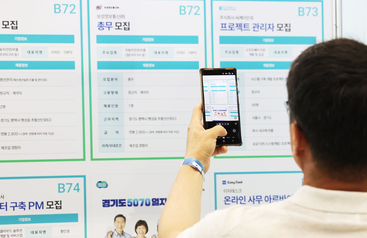 A job seeker photographs a recruitment board at a job fair with his phone at the Gyeonggi-do 5070 Job Fair held at Suwon Messe in Gwonseon-gu, Suwon, Gyeonggi Province, on July 9. (Yonhap)]