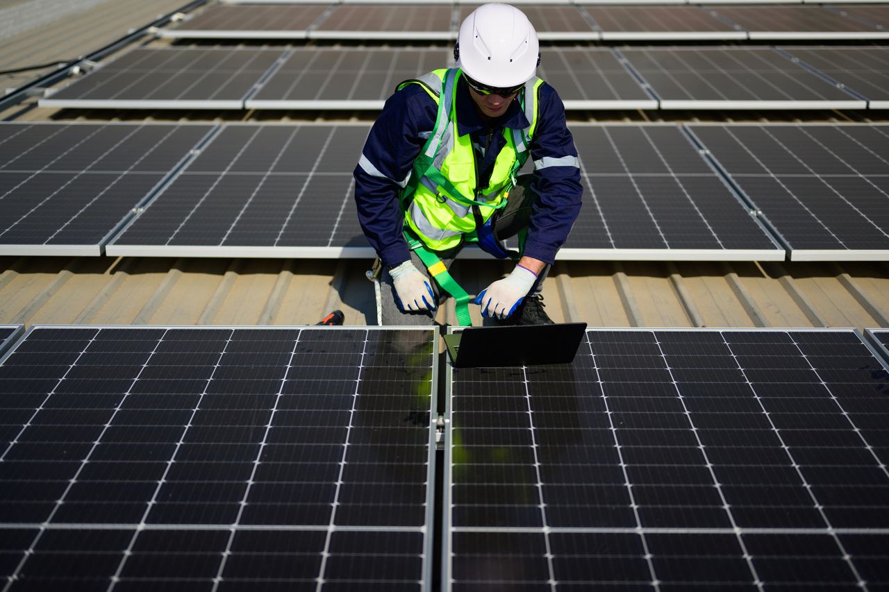 A technician uses a laptop to check and operate the system on the rooftop of a solar cell farm power plant. (123rf)]