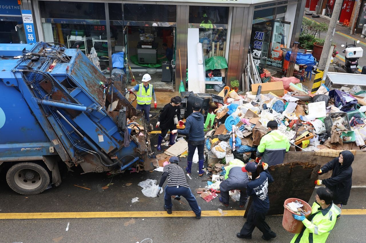 Workers clear piles of flood-damaged items from storefronts in Dangjin’s traditional market on Friday following heavy rain earlier in the week. (Yonhap)