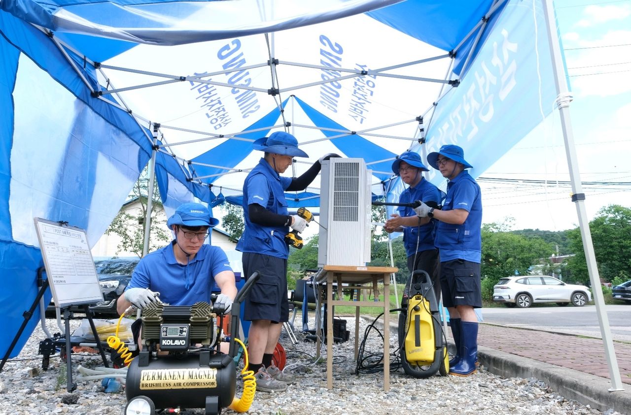 Samsung Electronics employees inspect and repair damaged home appliances in a flood-hit area. (Samsung Electronics)]