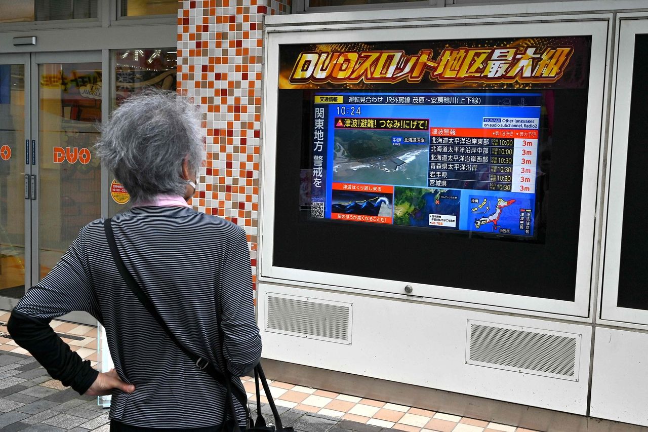 A woman watches a television broadcast of a tsunami warning for much of coastal Japan following a 8.7 magnitude quake in the sea off eastern Russia, outside a gaming shop in central Tokyo on Wednesday. (AFP via Yonhap)]