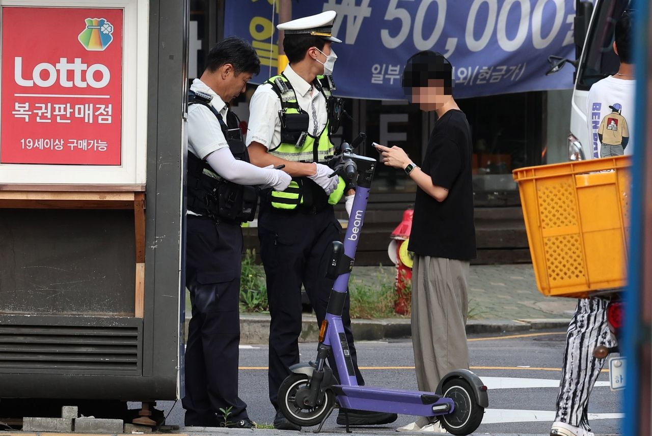 Police officers in Seoul’s bustling Seongdong-gu stop an e-scooter rider near Seongsu Station in August during a crackdown targeting helmet violations and rider safety. (Newsis)