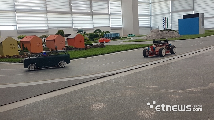 '2025 KAIST 모빌리티 챌린지 경진대회' 경기장에서 소형 차량이 무선통신을 통해 데이터를 받으면서 미니어처 도시의 도로를 주행하고 있다.