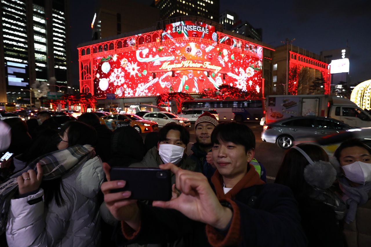Passersby take photos in front of a Christmas-themed video displayed on the media facade of Shinsegae Department Store in Myeong-dong, central Seoul. (Getty Images)