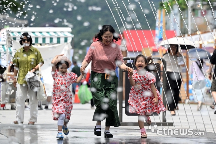 전국 대부분의 지역에 폭염 특보가 발령된 23일 서울 종로구 광화문광장 분수대에서 한 가족이 분수 터널을 지나고 있다. 기상청은 이날 서울 낮최고기온이 33도에 이를 것으로 예보했다. 김민수기자 mskim@etnews.com