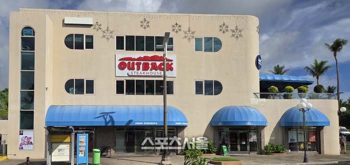 괌 투몬 거리 한복판에서 만난 아웃백 스테이크하우스. 이국적인 야자수와 어우러진 익숙한 브랜드 간판이 한국 여행객들에게 묘한 반가움을 선사한다. 괌 | 원성윤 기자 socool@sportsseoul.com