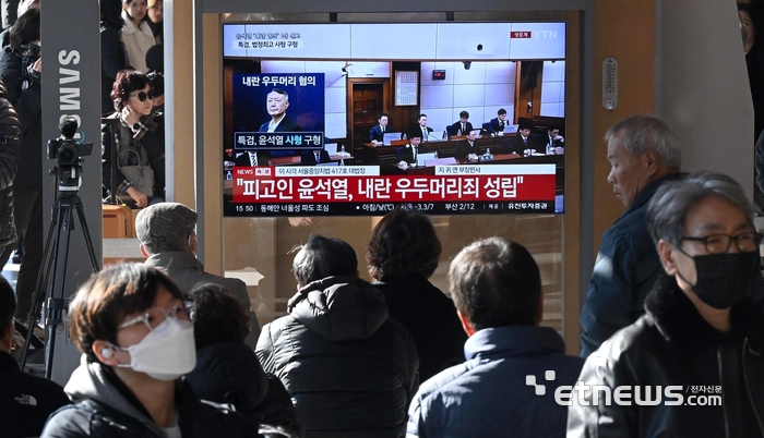 19일 서울 용산구 서울역 대합실에서 시민들이 윤석열 전 대통령의 내란 우두머리 혐의 사건 선고공판 생중계 영상을 시청하고 있다. 이동근기자 foto@etnews.com