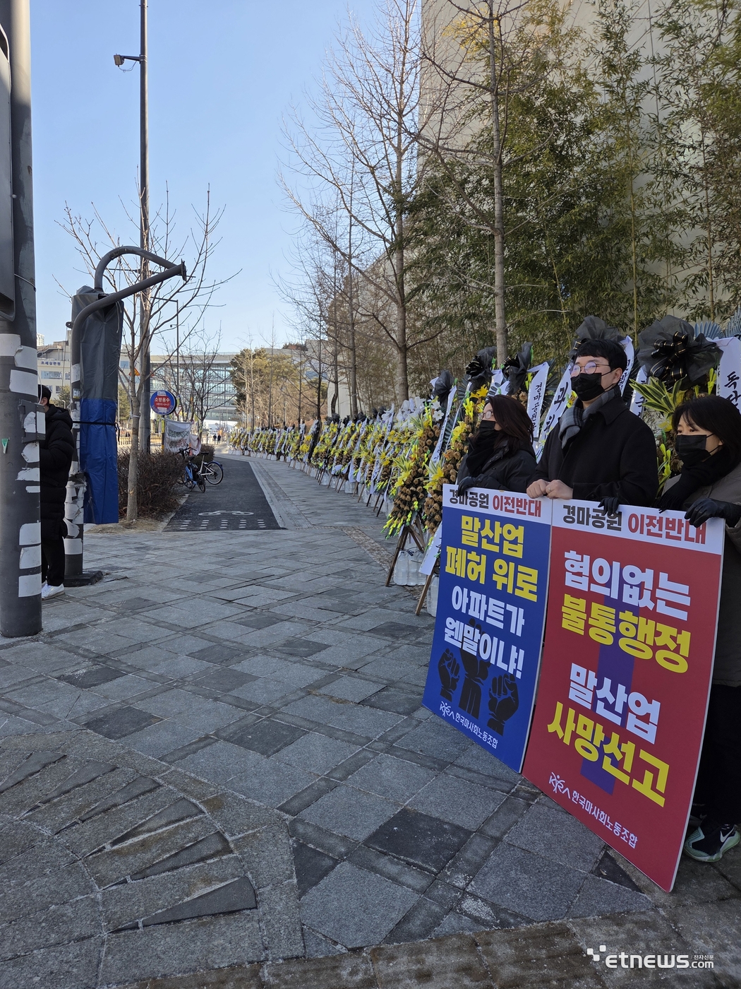 과천 경마공원(렛츠런파크) 이전·개발에 반대하는 한국마사회 노동조합원들이 9일 세종정부청사 앞에서 피켓을 들고 항의하고 있다. 이들 뒤로는 과천 시민들이 보낸 근조 화환이 청사 인근 보행로를 따라 줄지어 설치돼 있다.