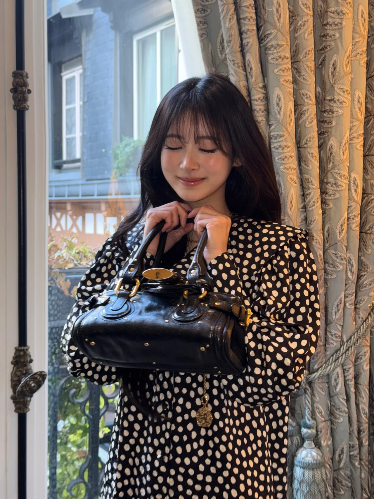 Anna completes a retro-feminine look with a black polka-dot dress and a gold-chain necklace. /Photo: MEOVV Instagram