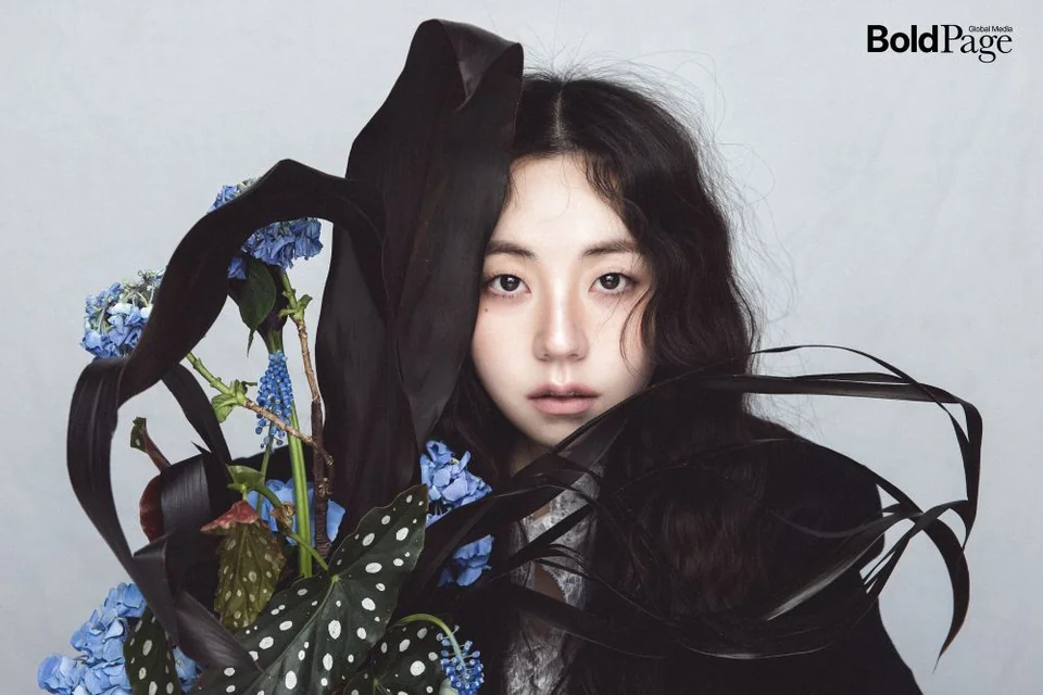 Ahn So-hee’s dark, moody portrait, styled with a black sheer top and fresh flowers / Photo: BoldPage