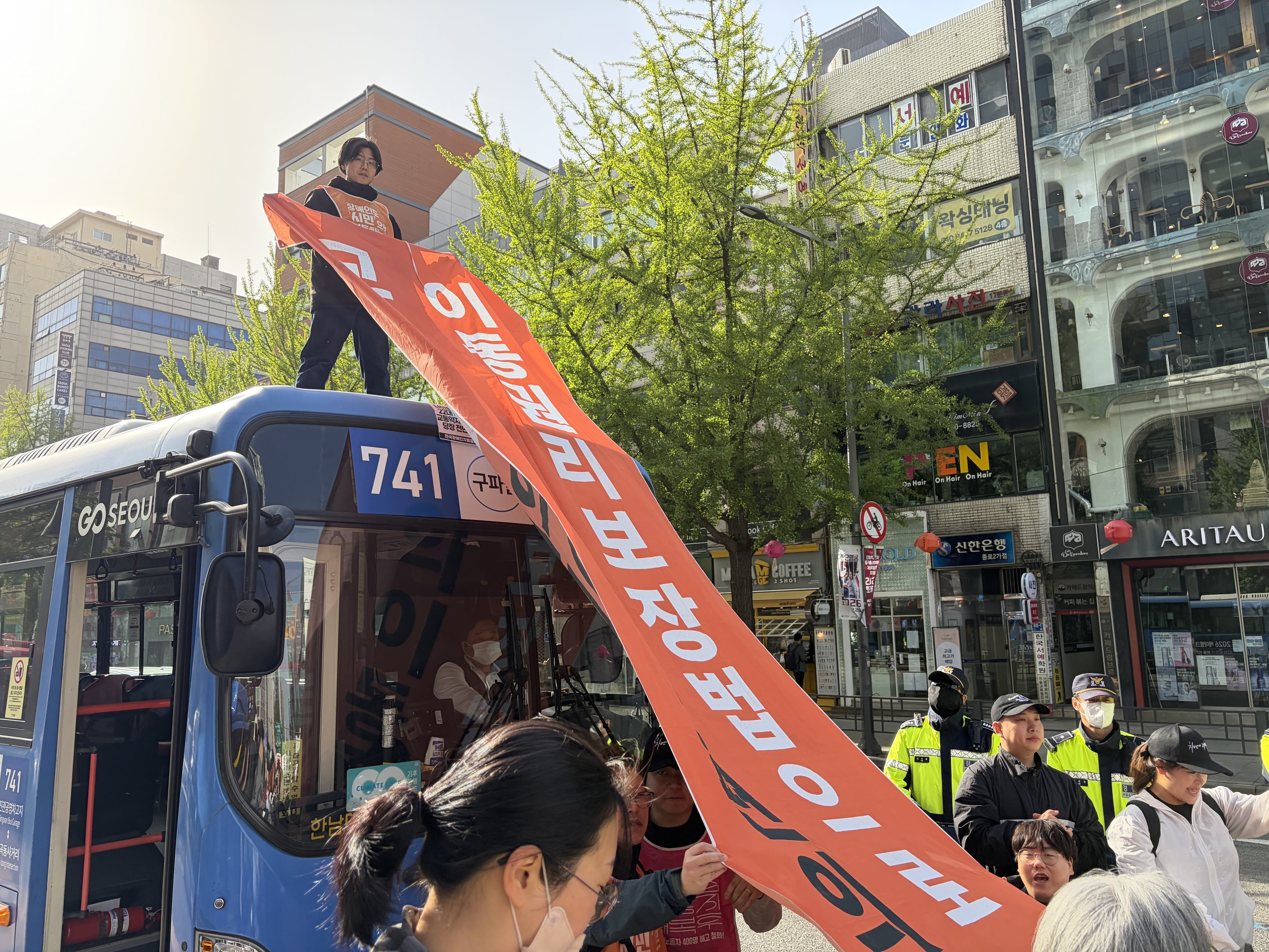 21일 서울 종로2가 일대에서 열린 전국장애인차별철폐연대(전장연)의 이동권 보장 촉구 시위에서 한 참가자가 버스 위에 올라 현수막을 펼쳐 들고 있다. /연합뉴스