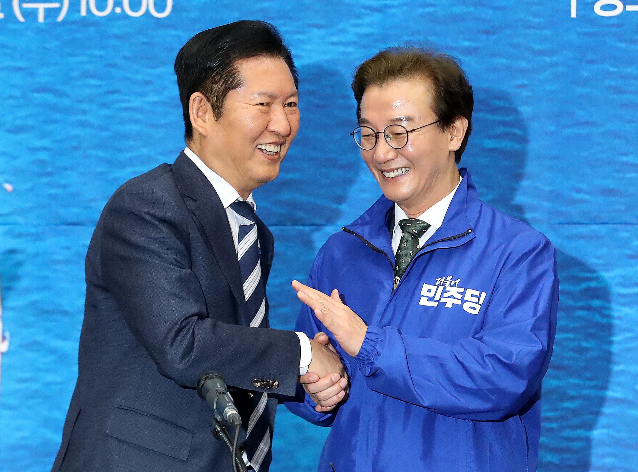 정청래 더불어민주당 대표가 15일 부산 동구 부산항국제전시컨벤션센터에서 열린 부산 현장 최고위원회의에서 전재수 부산시장 후보에게 당 점퍼를 입혀준 뒤 악수하고 있다./뉴스1