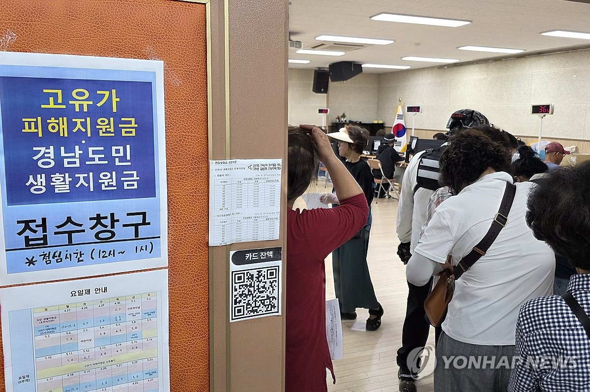 고유가 지원금, 이틀 만에 1000만 명 돌파… 고유가 지원금 신청 첫날, 주민센터 앞에 줄선 시민과 안내 표지판이 보이는 현장 사진