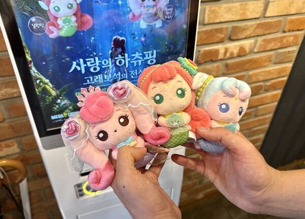 고객이 메가MGC커피 매장에서 ‘캐치 티니핑’ 극장판 ‘사랑의 하츄핑: 고래보석의 전설’ 공식 굿즈를 들어 보이고 있다 [사진=메가MGC커피]